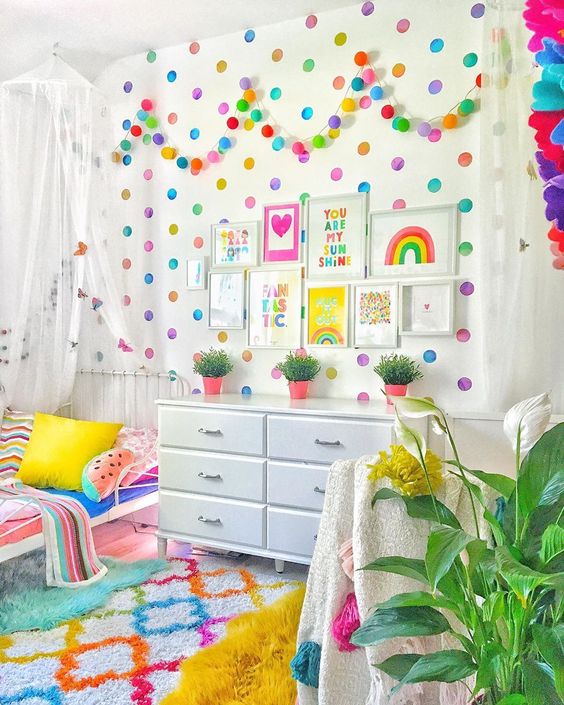 a colorful kid's space with a polka dot wall, a bold garland, bright bedding and fruit pillows and a bold rug just wows