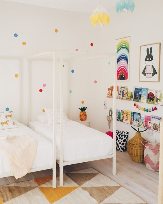 a shared kid's room done in neutrals but spruced up with brights - polka dots on the wall, colorful art, garlands and books