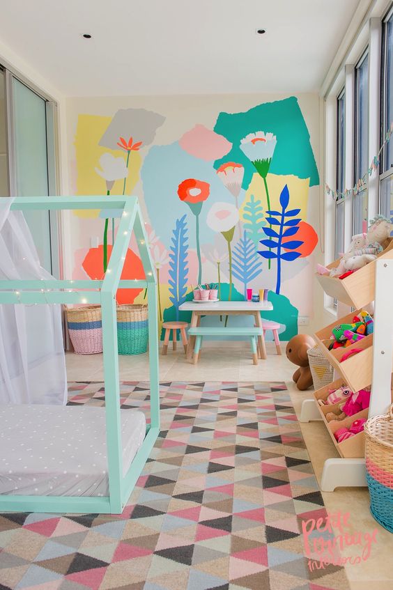 a pastel kid's room with a bright floral wall, a mint house-shaped bed, colorful toys and a bold rug and baskets