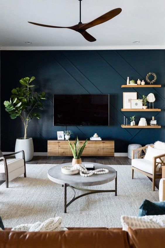 a cool living room with a navy paneled accent wall, wooden furniture, a catchy round table and greenery in pots