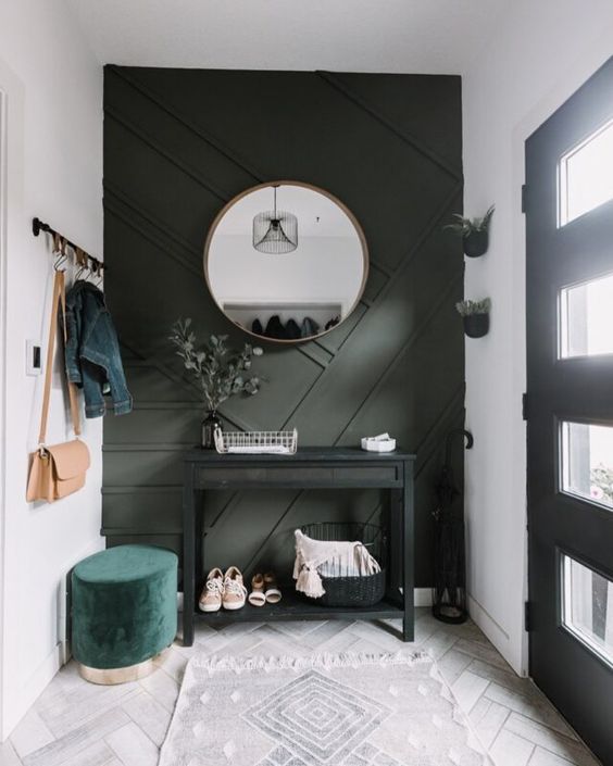 a small modern entryway with a dark green geometric wall, a black console, a green ottoman and potted greenery